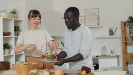 Wife-Putting-Salad-on-Plate-for-Husband-in-Kitchen